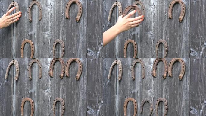 女孩手把复古生锈的马蹄铁放在古老的木制乡村房屋墙上。特写。