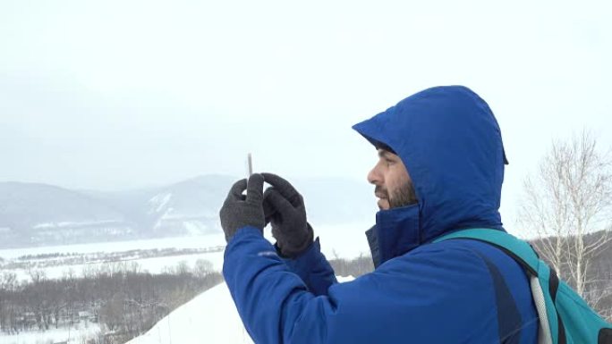 在山上使用智能手机的胡须旅行者。穿着夹克的白人男子在寻找全球定位系统信号。登山者冬季移动通信。冒险探