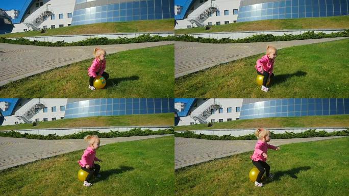 慢动作: 三岁的女孩在草坪上的橡皮球上跳。