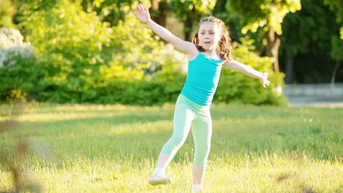 运动的小女孩在夏季公园的草地上做侧手轮。