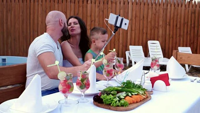 全家福照片让手机被放在一根棍子上自拍，父母带着孩子欢快的聚会，晚餐户外在一圈亲戚的人，幸福的家庭