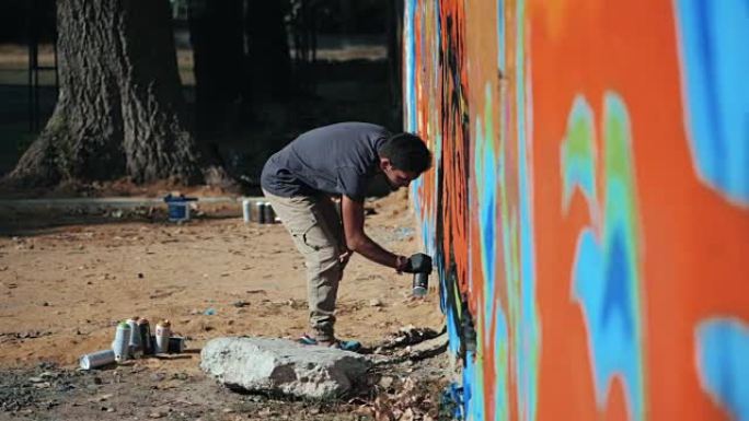 涂鸦艺术家用气溶胶作画。拿着喷雾器的人。缓慢的运动。年轻的城市画家在夏日的阳光下，在城市的街道墙上画