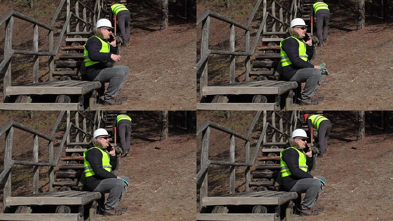 工人坐在木制轨道上并在智能手机上聊天