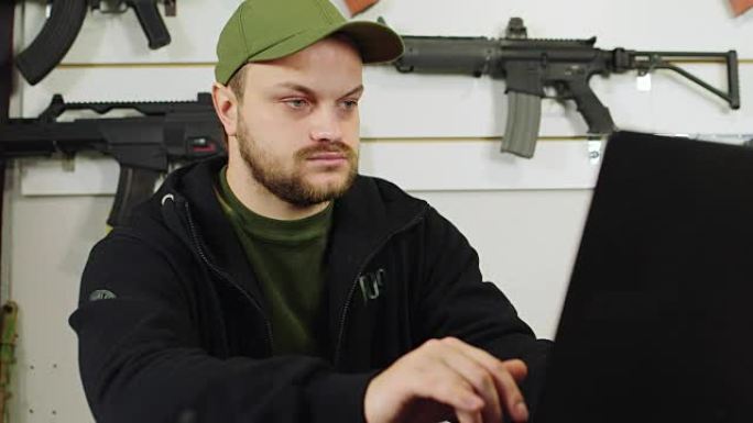 武器销售者用一台笔记本电脑检查店里的货物。在陈列柜的背景下，还有软气武器的样本