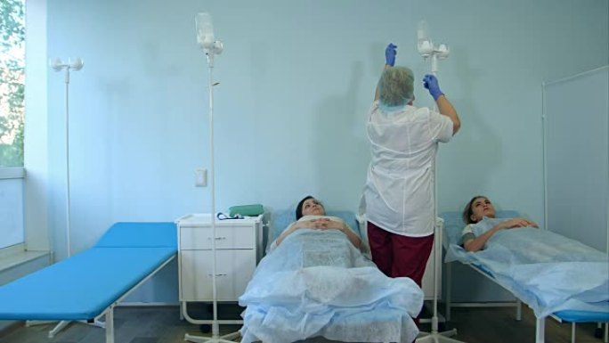 戴着口罩和手套的护士为病房的女性患者准备点滴