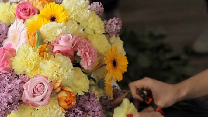 现代花店将淡黄色的康乃馨放在一束郁金香，紫丁香，玫瑰和其他五颜六色的花朵中