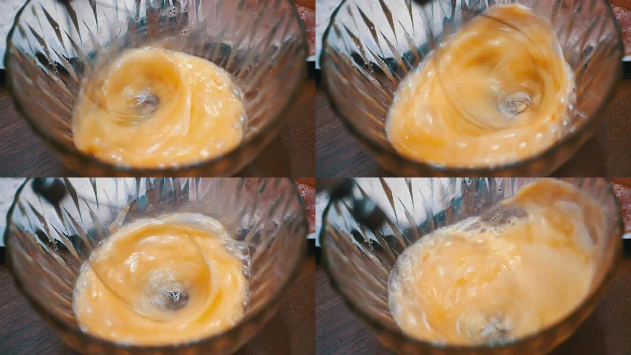 在带有电动手动搅拌器的透明碗中以慢动作搅打鸡蛋