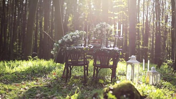 婚礼装饰的桌子在森林里为两个人设置。白玫瑰花束和带灯笼的老式蜡烛的婚礼装饰。