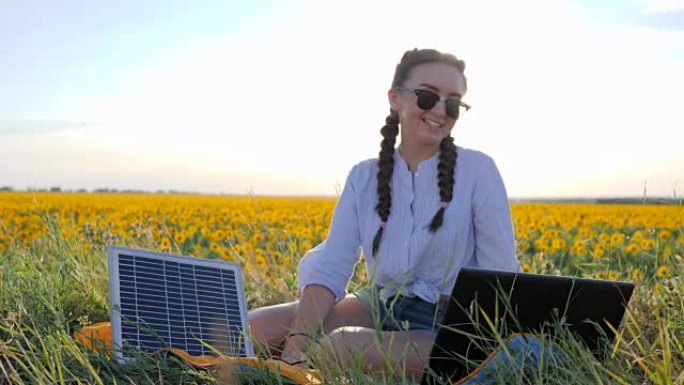 耗能技术，女孩在向日葵领域使用太阳能电池在笔记本电脑上聊天，年轻女子在使用太阳能电池
