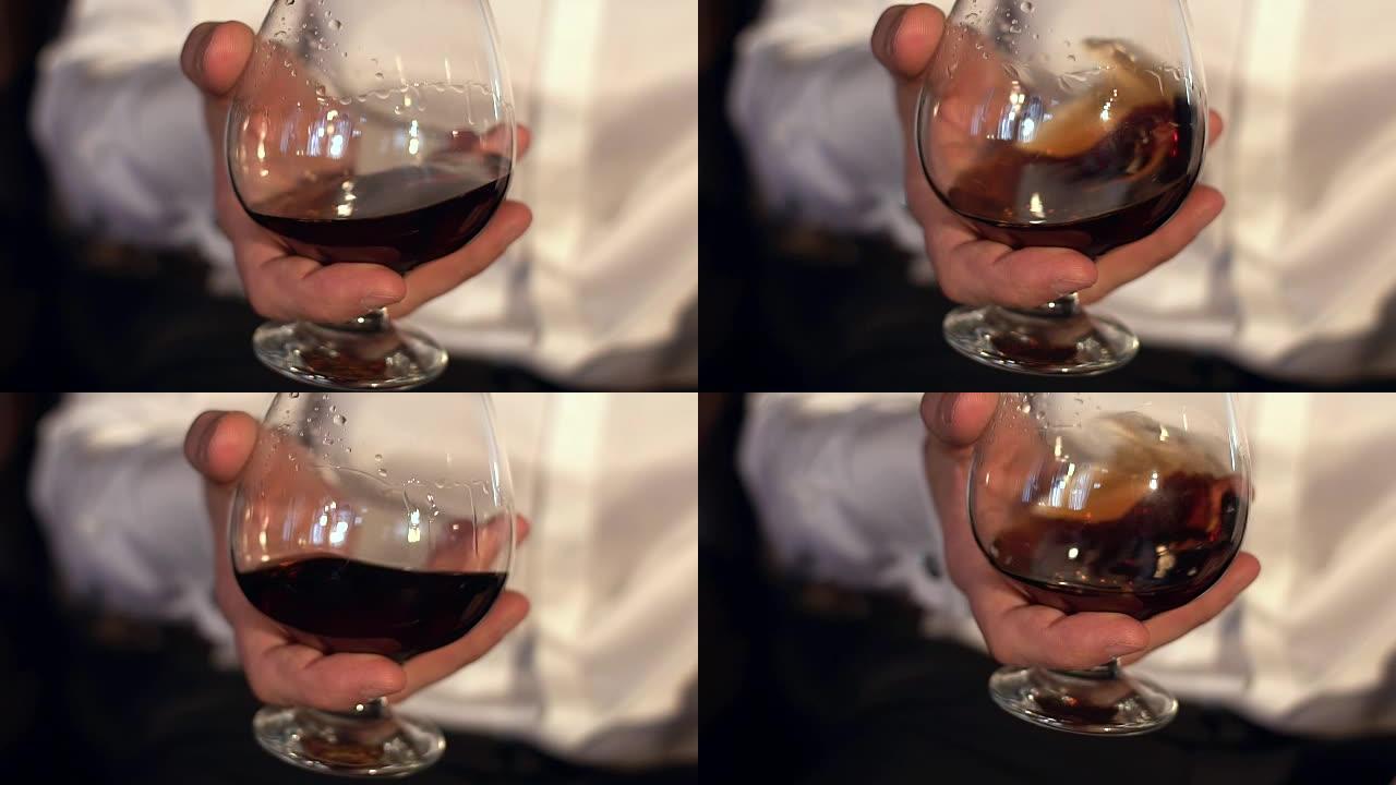 男人在玻璃杯中慢慢搅拌干邑白兰地，慢动作。男性手中的一杯威士忌。