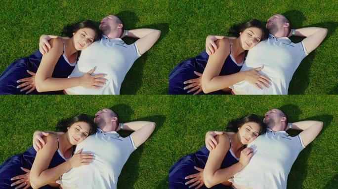 俯视图: 一个男人带着怀孕的妻子躺在绿草地上