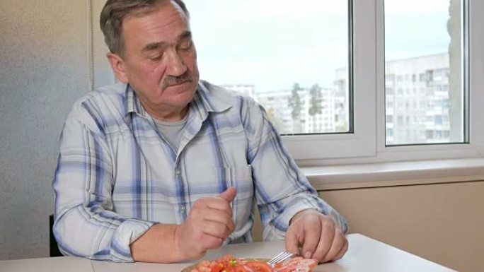 老年妇女在家里的厨房里给丈夫送蔬菜沙拉。她用叉子把一盘切成薄片的西红柿放在桌子上