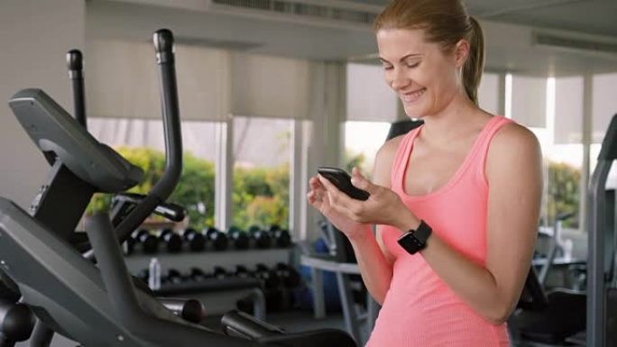 适合活跃的运动女性在速度模拟器上锻炼。使用她的智能手机，与朋友发信息