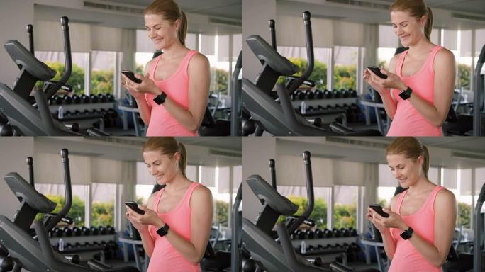 适合活跃的运动女性在速度模拟器上锻炼。使用她的智能手机，与朋友发信息