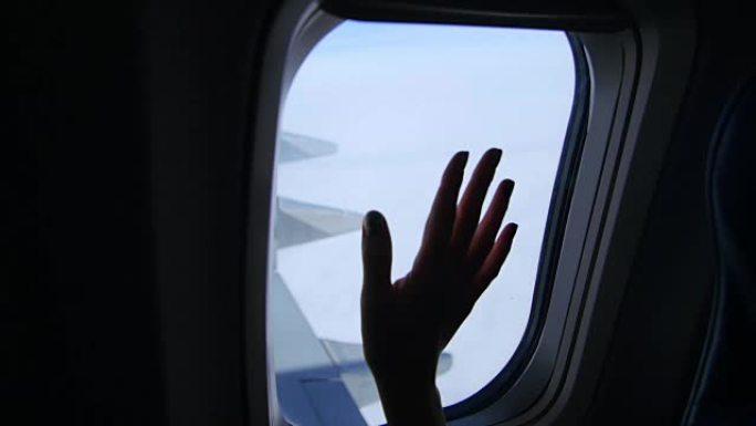 从飞机窗户看，你可以看到女性手、手掌、手指的运动、天空、云彩、飞机的翅膀的黑暗轮廓。天气晴朗，阳光明