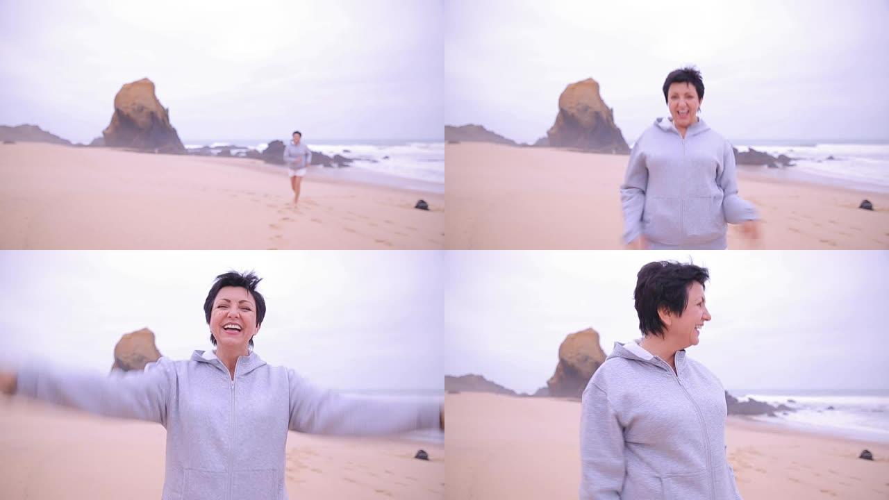 迷人的活跃的成熟女人沿着海洋海滩奔跑，对着镜头微笑。