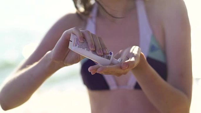 美容女孩在海滩上用瓶子里的防晒霜为身体涂防晒霜