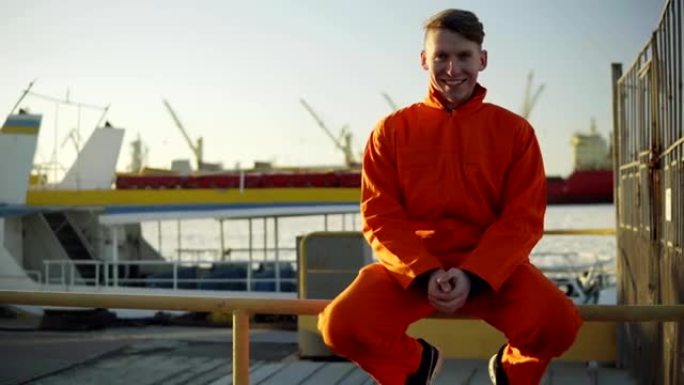 在港口的海边休息期间，一个穿着橙色制服的年轻人坐在篱笆上