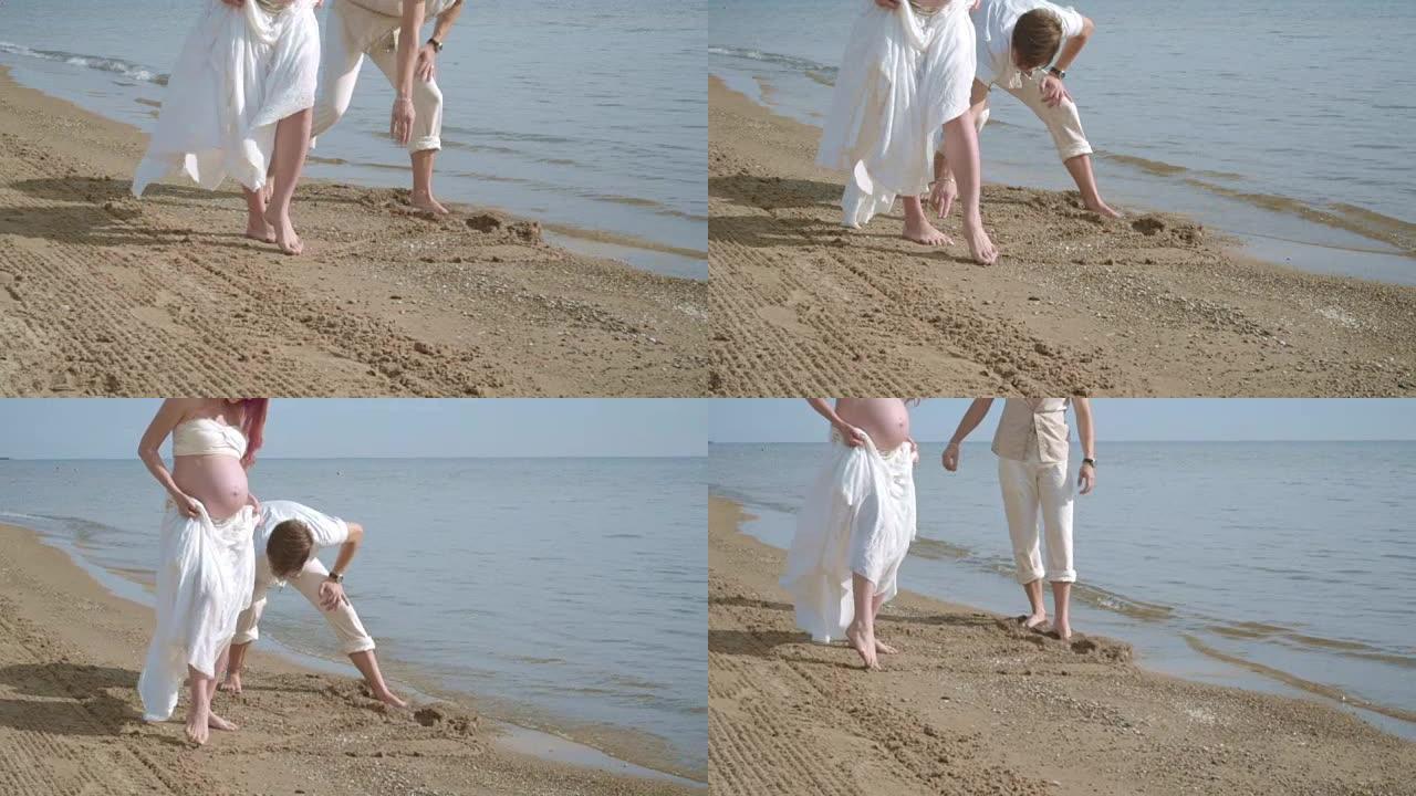 怀孕的夫妇在海滩上玩得开心。海滩上的情侣脚