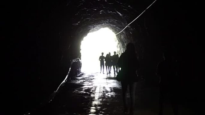 人们的轮廓穿过黑暗的隧道进入发光的尽头。自由和解决方案概念