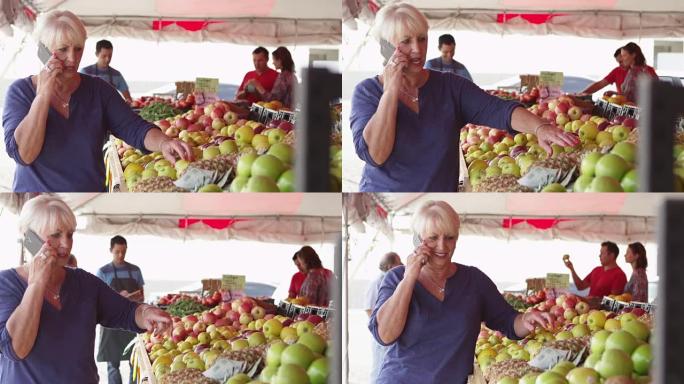 手机上的老年妇女在市场上购买新鲜水果