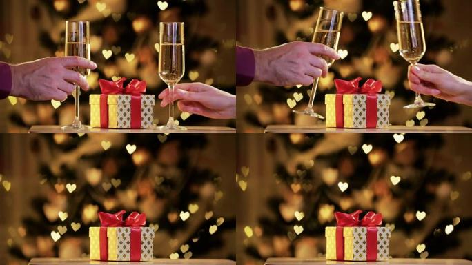 男性和女性的手，带有香槟杯和金色礼品盒，背景为节日灯光。