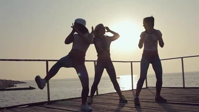 三个才华横溢的年轻女孩在日落时在海边的码头上跳舞表演