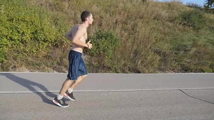 年轻的壮汉在美丽的大自然中奔跑。日落时分，男性跑步者在乡间小路上进行慢跑训练。英俊的运动男性在夏天的