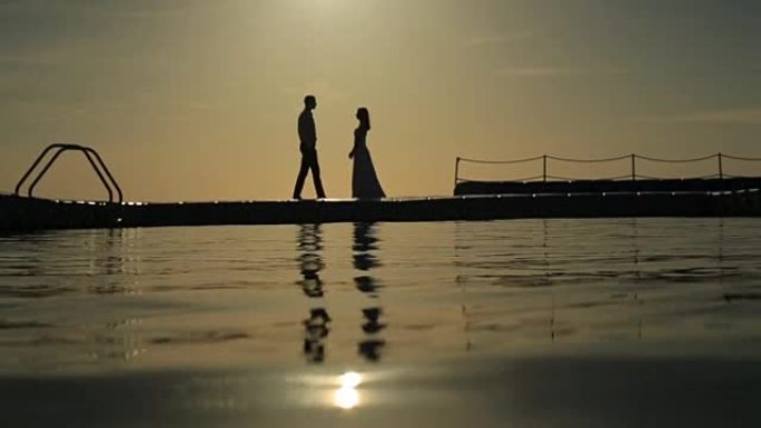 日落时分，浪漫的婚礼情侣走在泊位上的剪影。埃及的蜜月