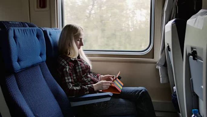 年轻女子乘火车旅行时在彩色盒子里使用平板电脑
