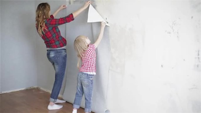 穿着格子衬衫的母女俩正在尝试在墙上贴上新的墙纸。