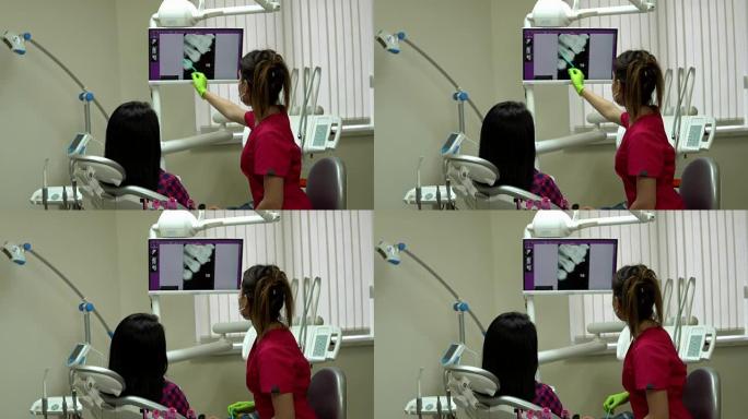 年轻的女医生用x光指着屏幕，解释她的病人需要治疗。年轻的女人坐在牙医的椅子上，看着监视器。4k拍摄