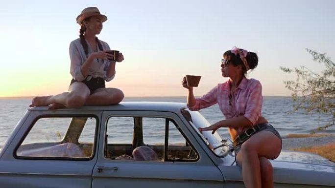 日落路堤上的美女茶会到汽车引擎盖，女友喝茶