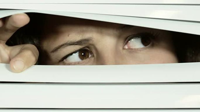棕色眼睛的女孩打开白色的百叶窗，从一侧到另一侧，表情不赞成，可疑。