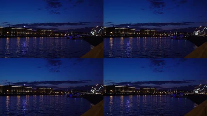 蓝色小时。河上的夜市灯光。海滨城市公园的景色。光线明亮的小船飘过。行人走在傍晚的长廊上。夜间汽车交通