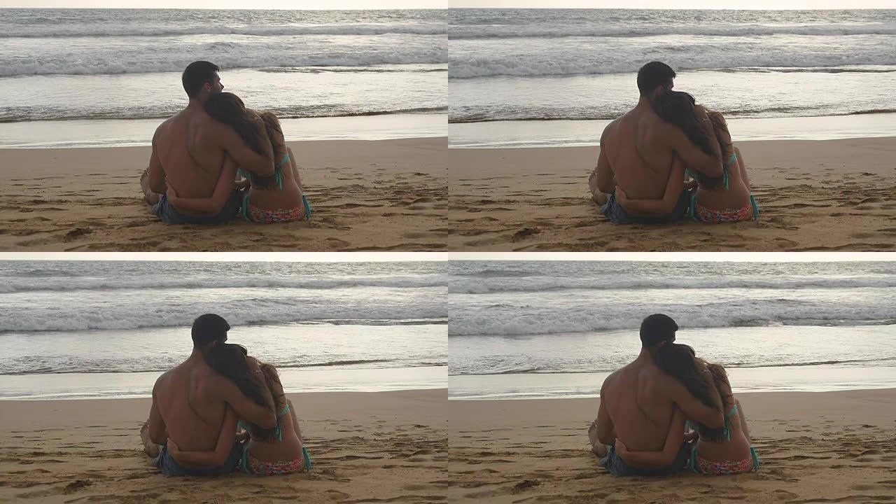 年轻浪漫的夫妇正坐在沙滩上拥抱着美丽的日落。一个女人和一个男人一起坐在海边的沙滩上，欣赏海洋和风景。