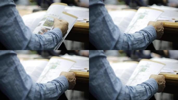 一个人坐在会议上翻阅一本有图表和图纸的杂志