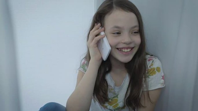 美丽快乐的小女孩情绪激动地在窗前的智能手机上聊天