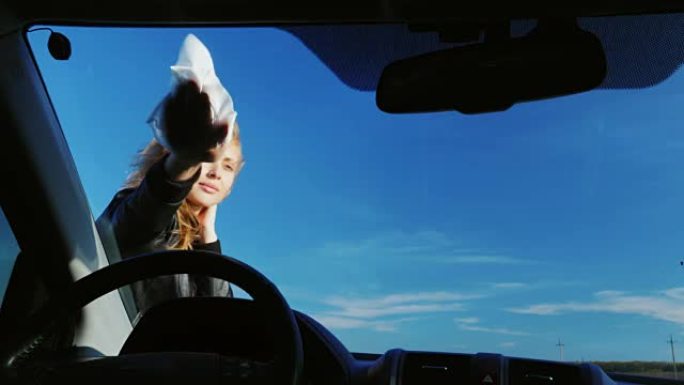 年轻迷人的女人在擦汽车的挡风玻璃。从车里看。在晴朗的日子里，以红蓝的天空为背景