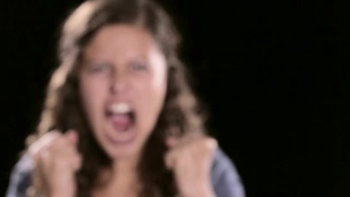 愤怒的年轻女子对着镜头发怒，挥舞着拳头大喊。