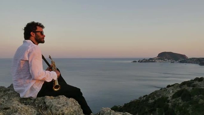 音乐家在日落时坐在海边的一个小岛上的悬崖边缘演奏萨克斯风