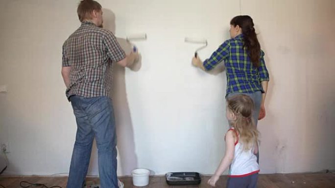 妈妈，爸爸，女儿的家人用画笔和滚筒涂漆墙。