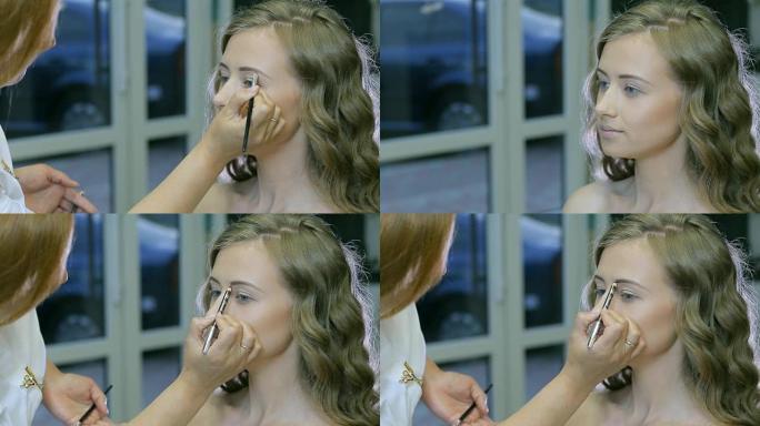 专业化妆师在金发模特眼睑上涂抹色调粉。