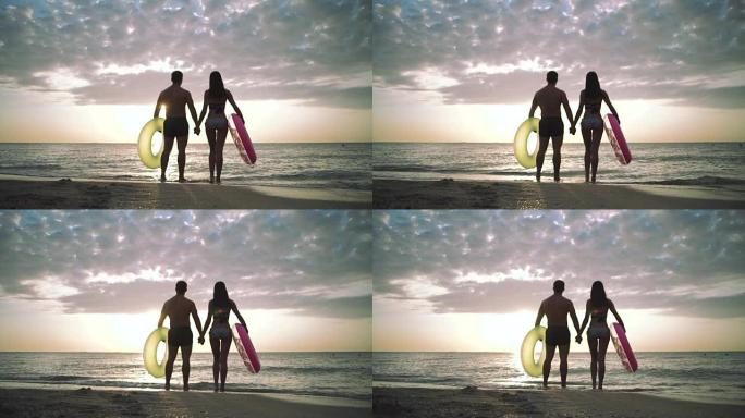 日落时海滩上年轻夫妇的剪影，带橡胶圈