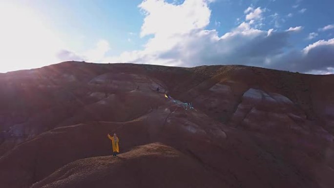 空中: 一个年轻的女孩站在红山上放风筝在高山上的背景。自由的想法，在山里寻找冒险。这个女孩梦想一个更