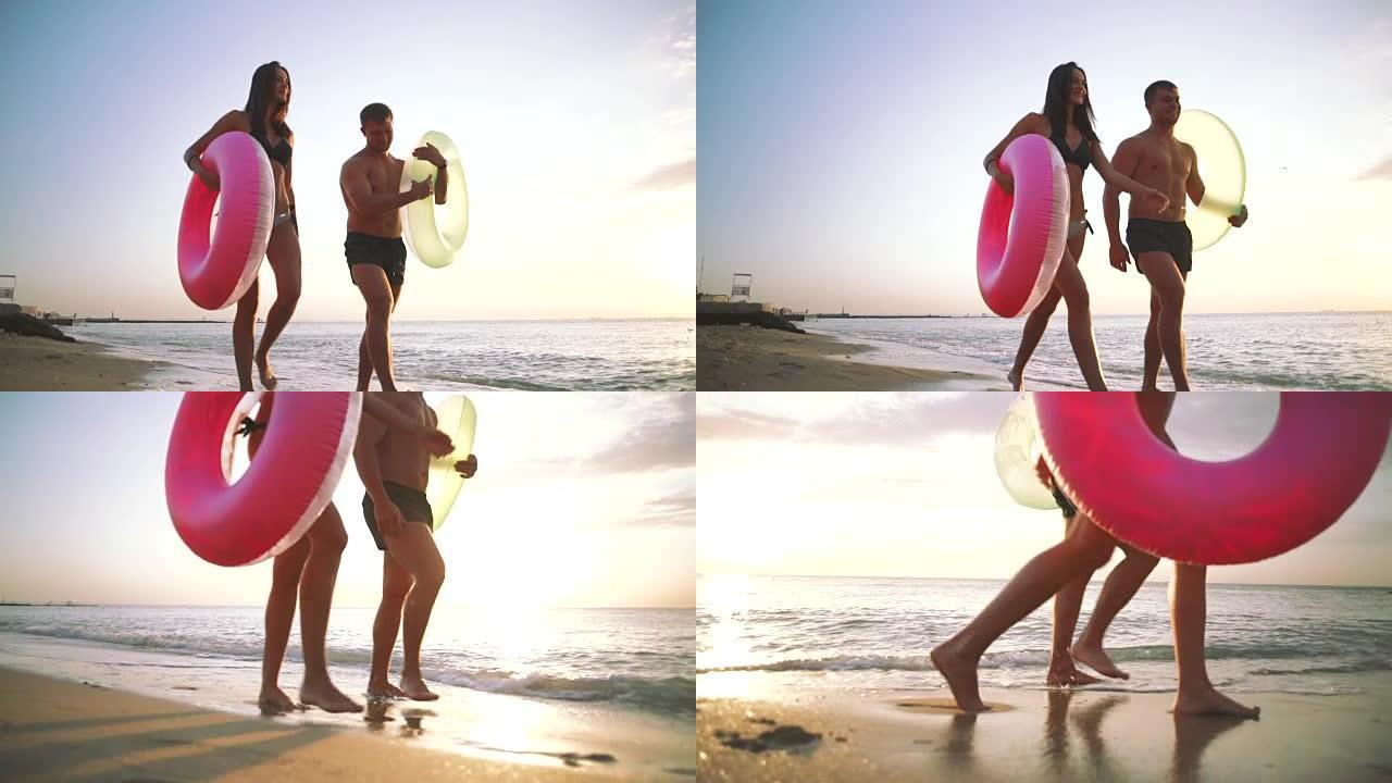 幸福的年轻夫妇在日落时带着橡胶圈在沙滩上散步，慢动作