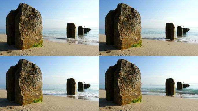 静态拍摄平静的平静海浪场景，用混凝土桩搭接在美丽的沙滩上