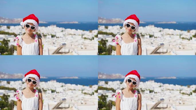 米克诺斯户外背景的白色连衣裙和红色帽子迷人女孩。孩子在希腊米科诺斯岛上典型的希腊传统村庄的街道上，白