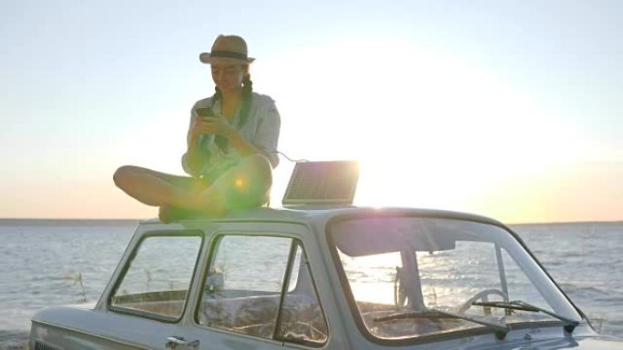 照片在阳光下的汽车上，女孩坐在背光的车顶复古车上，在手机上自拍