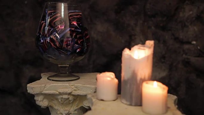 玻璃花瓶，巧克力，糖果和燃烧的蜡烛在前景。花瓶里的巧克力糖果和燃烧的蜡烛。花瓶里的巧克力糖果和糖果。